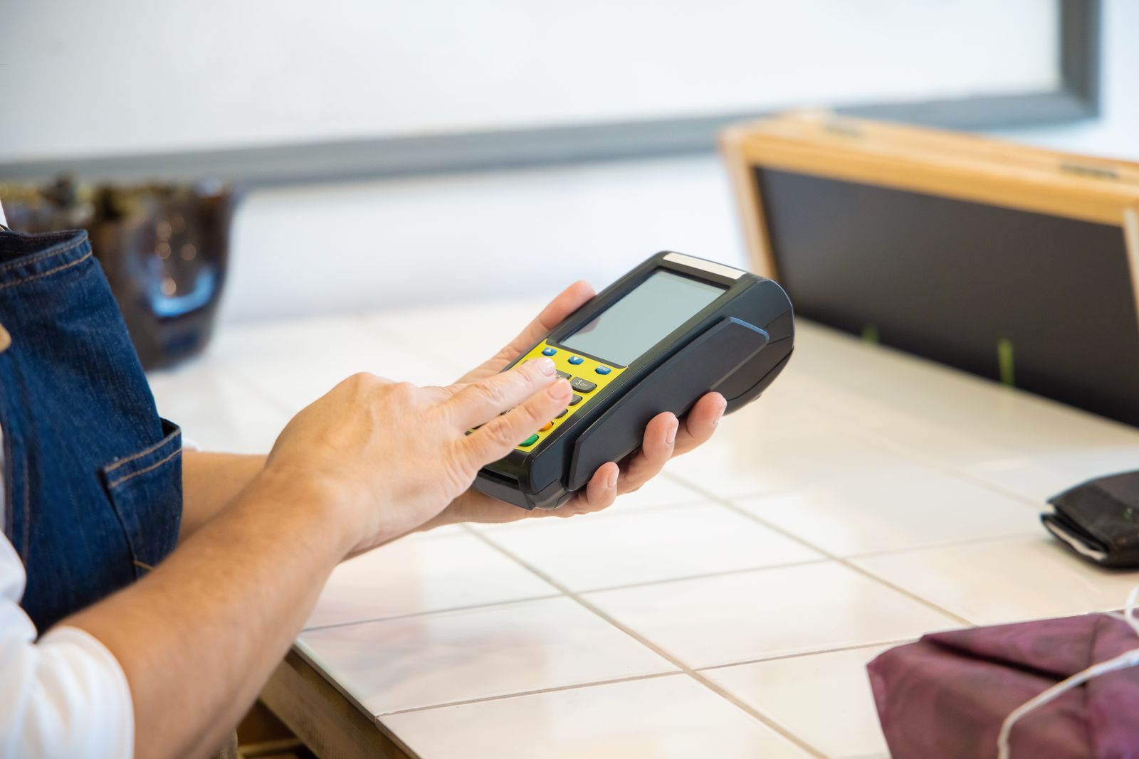 Merchant in an apron holding a card payment terminal at the counter
